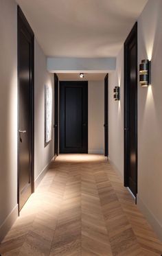 an empty hallway with black doors and wooden flooring is lit by recessed lights