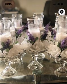 there are many glass vases with flowers in them on the table and one is filled with candles