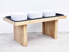 three white bowls are sitting on a black tray that is attached to a wooden stand