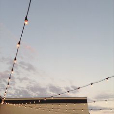 string lights are hanging from the side of a building at dusk with clouds in the background