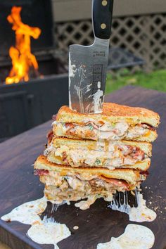 a stack of food sitting on top of a cutting board with a knife stuck in it