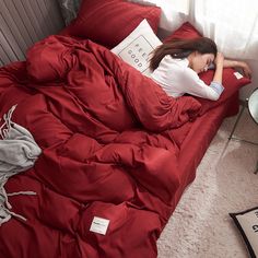 a woman laying in bed with red comforter and pillows on top of her head