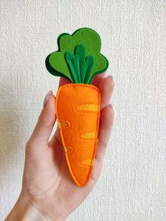 a hand holding a felt carrot with green leaves