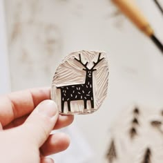 a person holding up a metal brooch with a deer on it's back