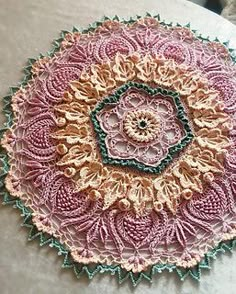 a crocheted doily is sitting on a white tablecloth with pink and green accents