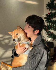 a man holding a small dog in his arms while sitting on a chair next to a christmas tree