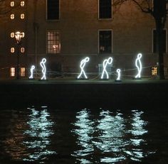 some lights are projected on the water in front of a building at night with people walking by