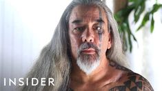 a man with long grey hair and tattoos on his face is looking at the camera