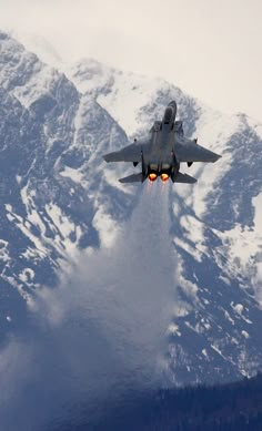 a fighter jet flying through the air over snow covered mountains