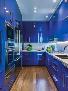 a blue kitchen with stainless steel appliances and wood floors is seen in this image from the front view