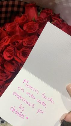 a person holding a piece of paper with writing on it in front of red roses