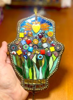 a hand holding a stained glass fan on top of a wooden table