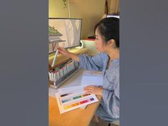 a woman is sitting at a desk with some papers and color pencils in front of her