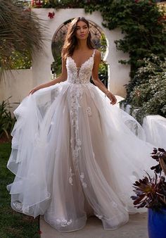 a woman in a wedding dress is standing on the sidewalk near some plants and flowers