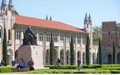 many people are walking around in front of a building with a statue on the lawn