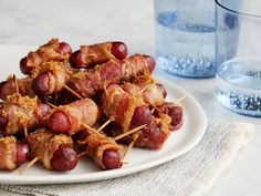 bacon wrapped hotdogs are on a white plate next to a glass of water