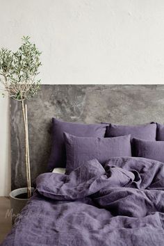 a bed with purple linens and a plant in a vase on the nightstand next to it