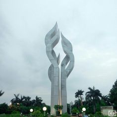 a large metal sculpture in the middle of a park with people sitting on benches around it