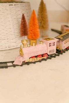 a toy train is on the tracks next to christmas trees