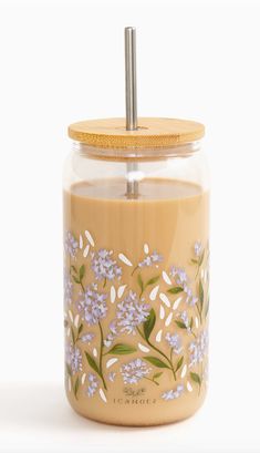 a glass jar with flowers painted on the side and a metal straw sticking out of it