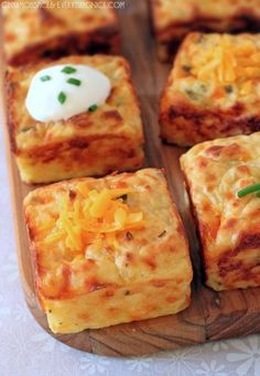 several square pieces of food on a wooden tray with cheese and sour cream toppings