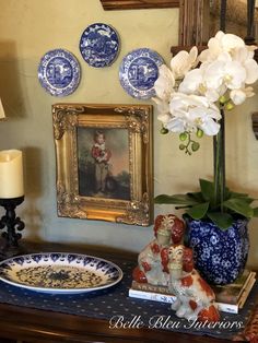 a blue and white vase with flowers on top of a dresser next to a painting