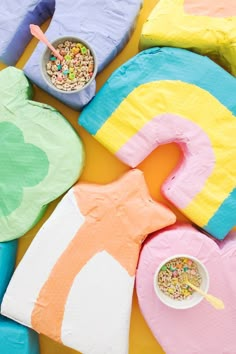 colorful paper mache shapes with cereal in bowls and spoons next to them on a yellow surface