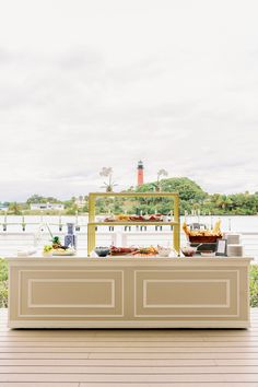 an outdoor buffet with lots of food on the table and water in the back ground