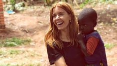 a woman holding a boy in her arms and smiling at the camera while standing outside