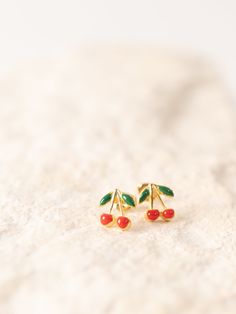 Add a touch of retro charm to your look with these delightful cherry stud earrings, inspired by the 90s rockabilly style and timeless vintage appeal. Size: .75" W x .75" H.Materials: 14K gold-plated brass with surgical steel posts. 100% made in the USA. Amano ("By Hand" in Spanish) is a small, woman-owned jewelry brand and zero-waste production studio in Sonoma California. A small team of women artisans and family members handcraft designs inspired by vintage fashion, the night sky, and the Gold Cherry Round Earrings For Gift, Cheap Cute Cherry Colored Earrings, Trendy Cherry Dangle Earrings, Cute Cheap Cherry-colored Earrings, Gold Cherry Earrings, Sonoma California, Ski Girl, Production Studio, Rockabilly Style