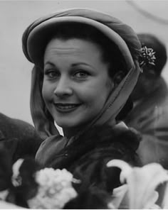 black and white photograph of a woman wearing a hat with flowers in her hair smiling at the camera