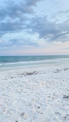 a surfboard sitting on top of a sandy beach next to the ocean under a cloudy sky