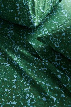 a close up view of a green bed sheet with white flowers on it and the sheets are folded down