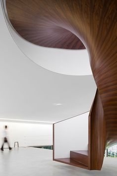 the inside of a building with people walking around it and a curved wooden structure in the center