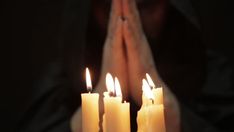 a person holding their hands in front of three lit candles with both hands folded over them