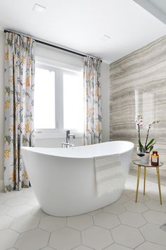 a white bath tub sitting in a bathroom next to a window with drapes on it