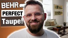 a man with glasses and beard standing in front of a living room filled with furniture