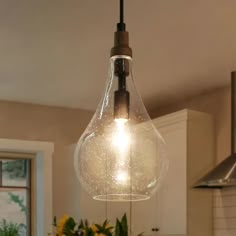 a light fixture hanging from the ceiling in a kitchen with flowers on the counter top