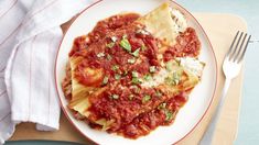 a white plate topped with lasagna covered in sauce and cheese next to a fork