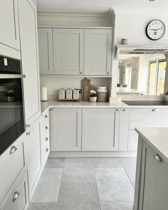 a kitchen with white cabinets and gray flooring is pictured in this image, there is a clock on the wall