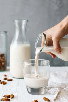 someone pouring milk into a glass with almonds on the table next to it,