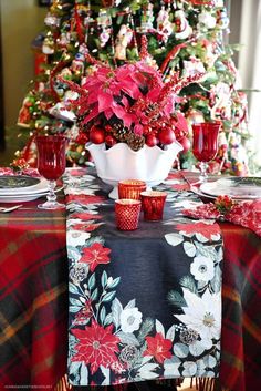 a christmas table setting with poinsettis, candles and red glasses on it