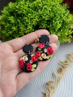 the hand is holding two black and red earrings with flowers on it's sides