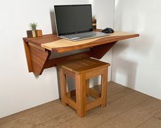 a laptop computer sitting on top of a wooden desk next to a stool and potted plant