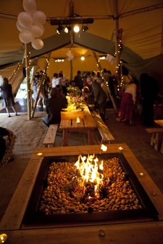 a long table with lit candles in the middle and people standing around it at an outdoor event