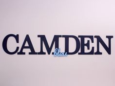 the word camden is cut out of blue paper and placed on a white wall in front of it