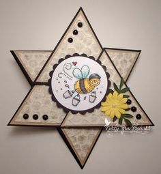 a star shaped card with a bee and flower on it's side, in front of a white wall