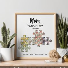 a framed puzzle piece with the words mom on it next to some succulents