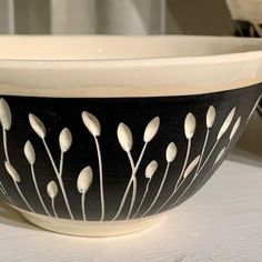 a black and white bowl with flowers painted on the side is sitting on a table