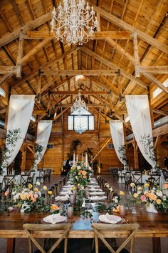 an indoor wedding venue with wooden tables and white drapes on the ceiling, decorated with floral centerpieces